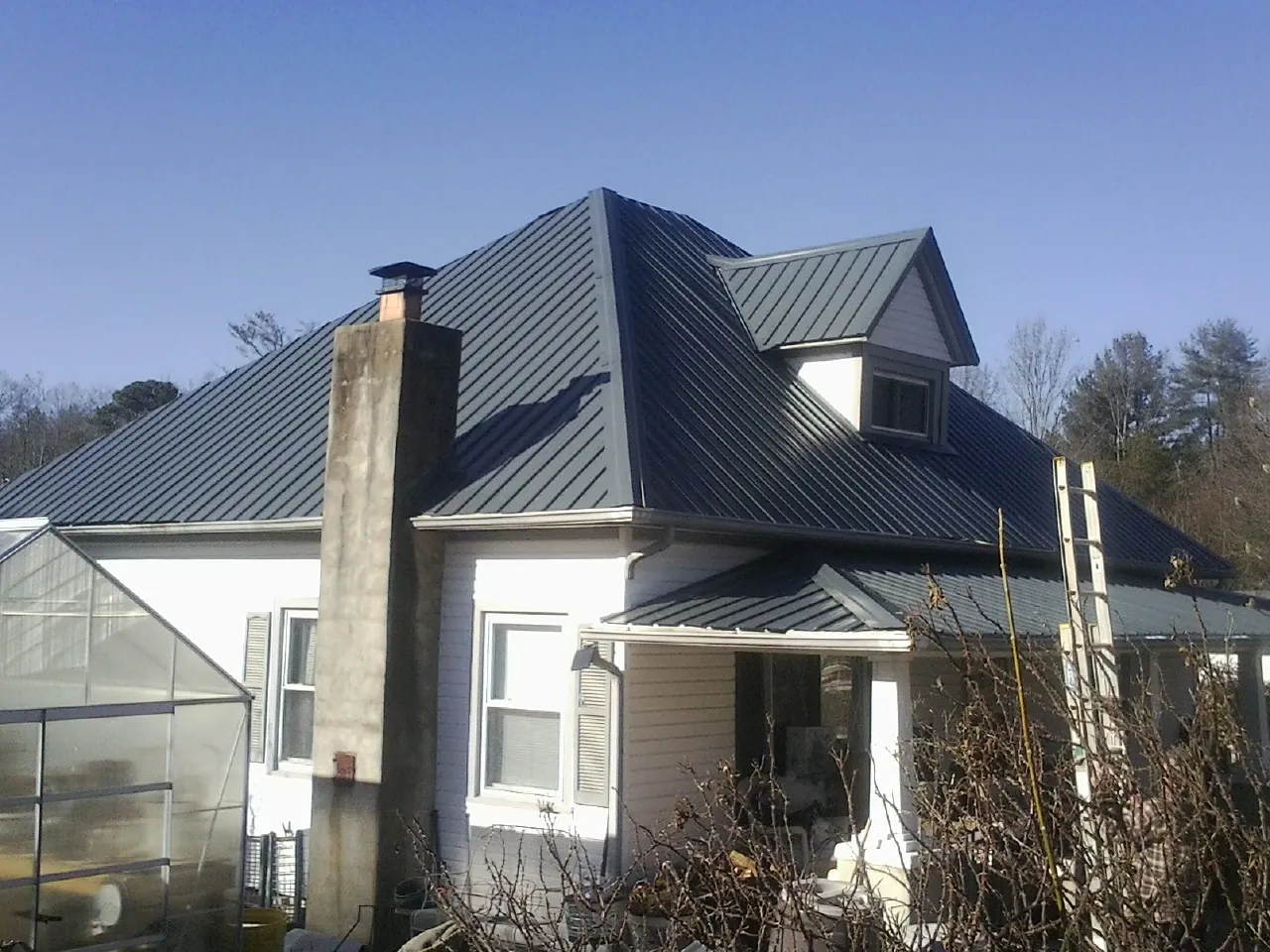 Dark blue standing seam metal roof on a white farmhouse with dormer — Slate & Tile Roof Repair by Roofing Brothers in Goldsboro