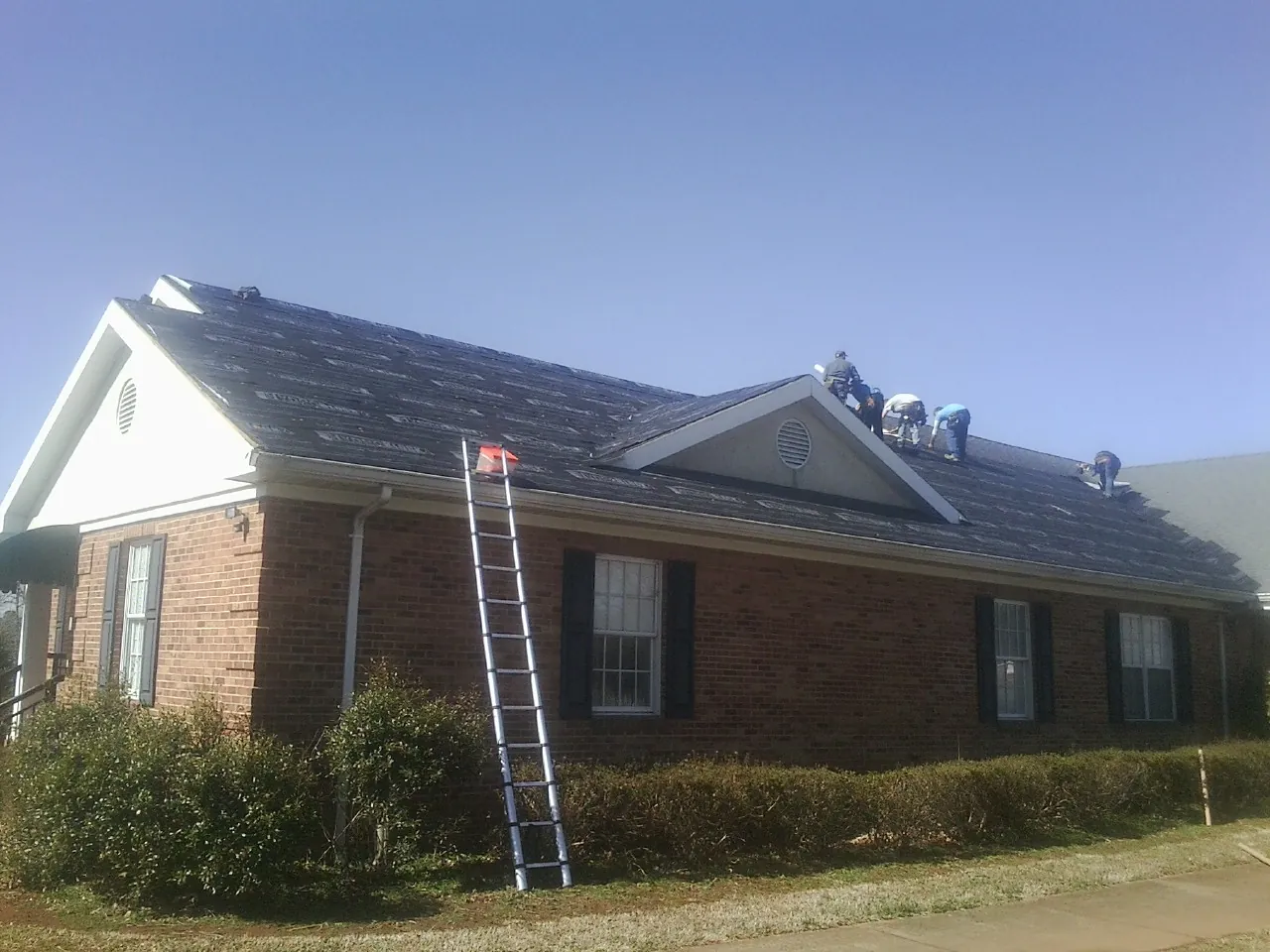 Crew tearing shingles off a brick ranch roof with a ladder set — Metal Roof Repair work by our crew in Goldsboro
