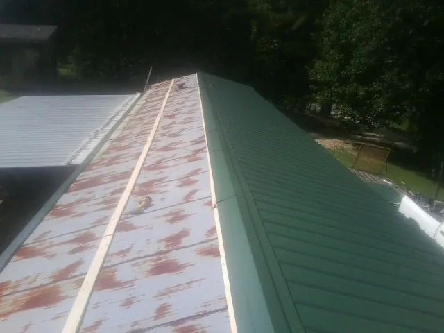 Old rusted panels beside newly installed green metal roofing — Wind Damage Roof Repair by Roofing Brothers in Goldsboro