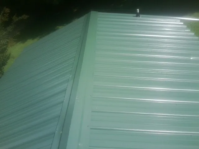 New green metal panels meeting at the ridge of a roof — Flat Roof Repair work by our crew in Goldsboro