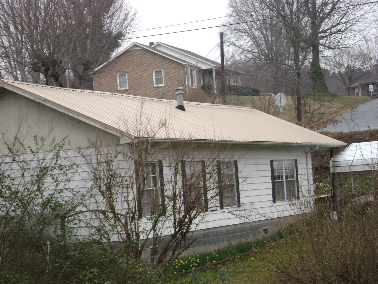 Tan metal roof on a white sided house set into a hillside — Commercial Roofing by Roofing Brothers in Goldsboro