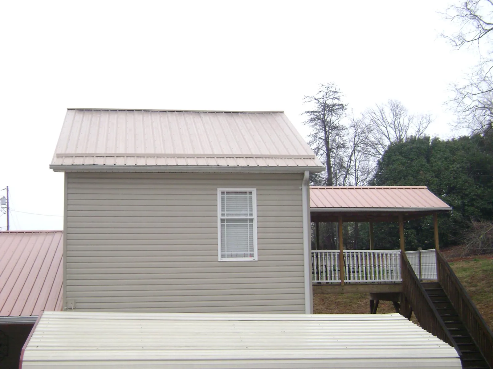 Tan metal roofs on a two story addition and attached porch, from a Roof Replacement job in Goldsboro
